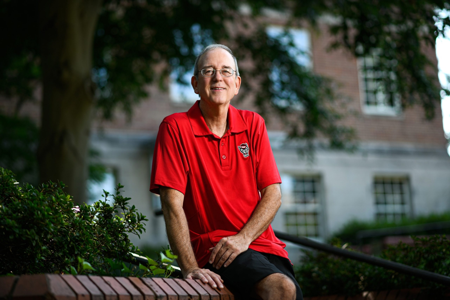 William O'Brien sits on a wall at NC State's campus in a red Wolfpack polo.