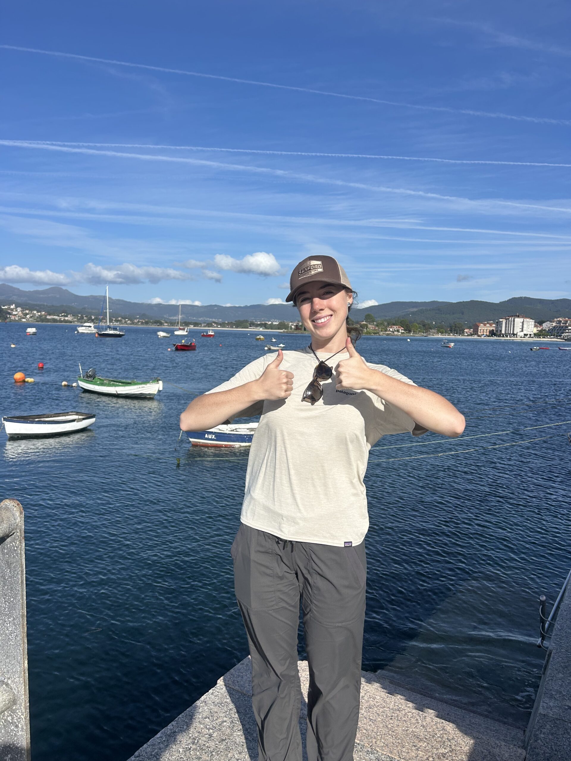 Delta holds up two thumbs up overlooking water with colorful boats.